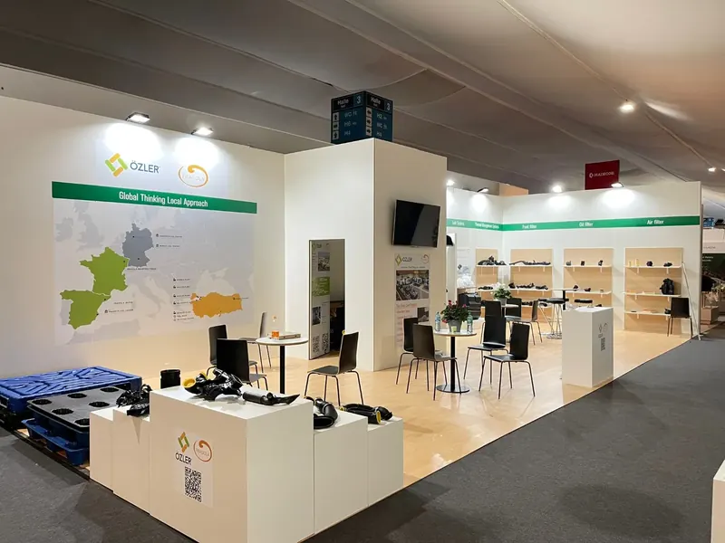 Weiß-grüner Messestand mit Kartengrafik, Produktpodesten und hellen Holzoptikflächen.