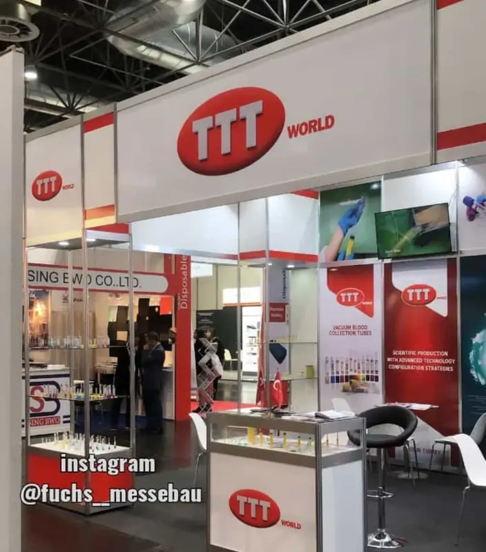 Weiß-roter Messestand mit hohen Schildern, Produktvitrinen und schwarzen Stühlen.
