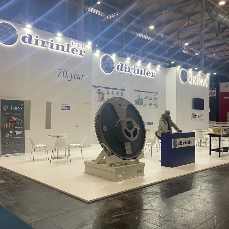 Weißer Messestand mit großem rundem Metallteil auf einem Podest und blauer Theke.