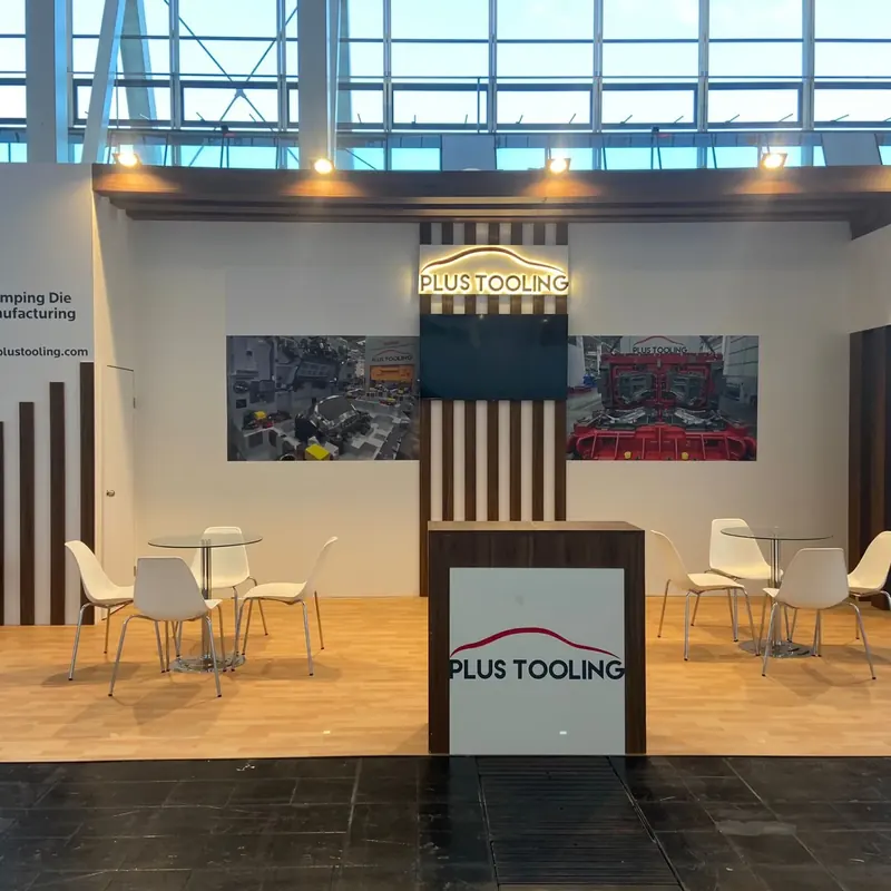 Weißer Messestand mit Holzlamellen, dunkler Empfangstheke und weißen Sitzgruppen auf Holzboden.