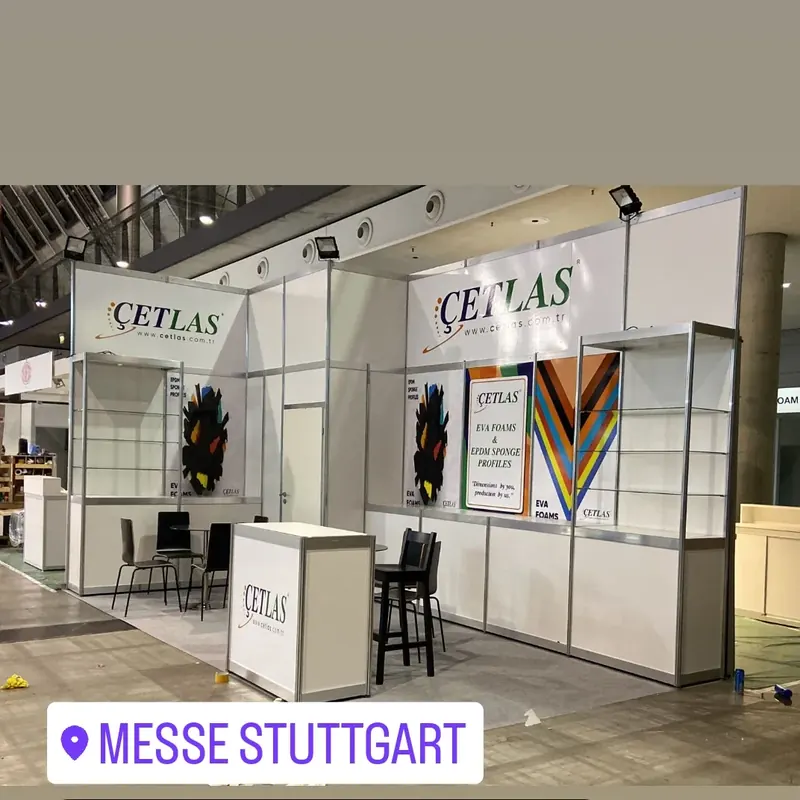Grauweißer Messestand mit diagonaler Farbgrafik, Produktregalen und kleiner Theke.