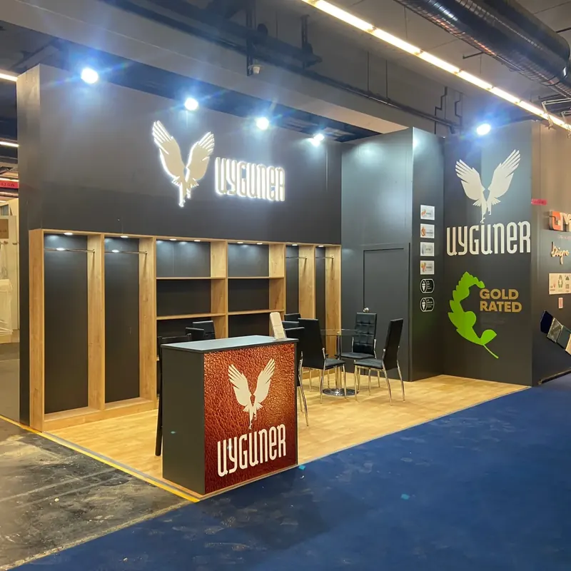 Schwarz-goldener Messestand mit Holzoptikregalen, Adlergrafik und schmaler Theke.
