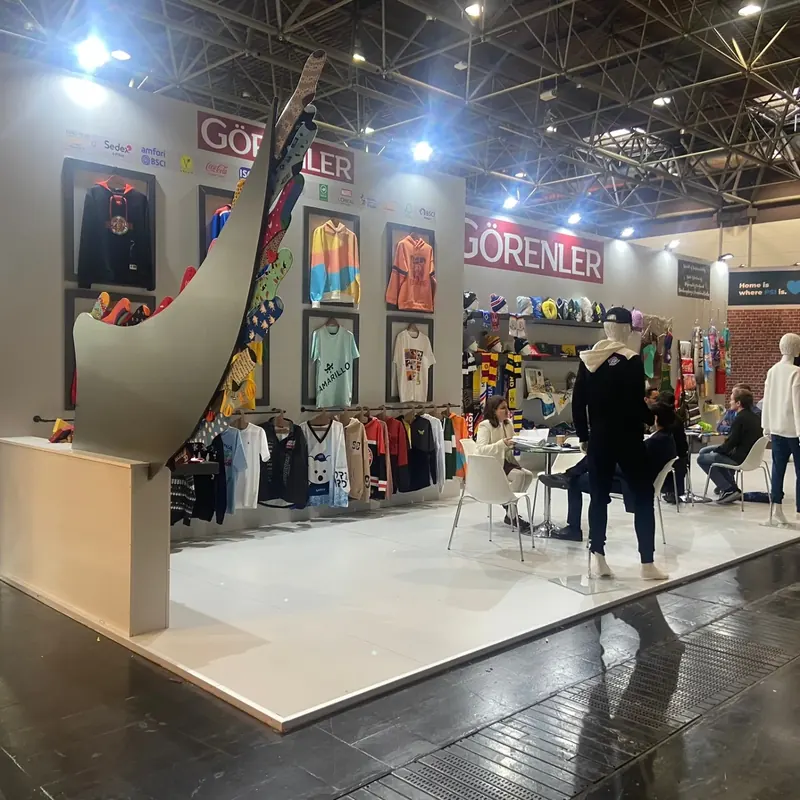 Heller Messestand mit bunten Bekleidungsmustern und hoher gebogener Präsentationsfläche.