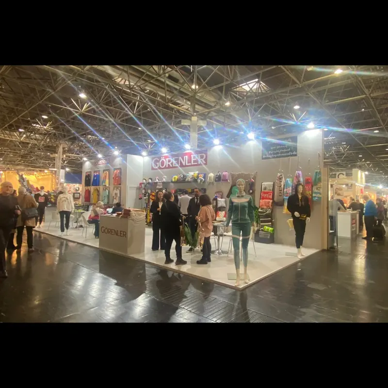Weißer Messestand mit bunten Textilien und mehreren Personen am Hallengang.