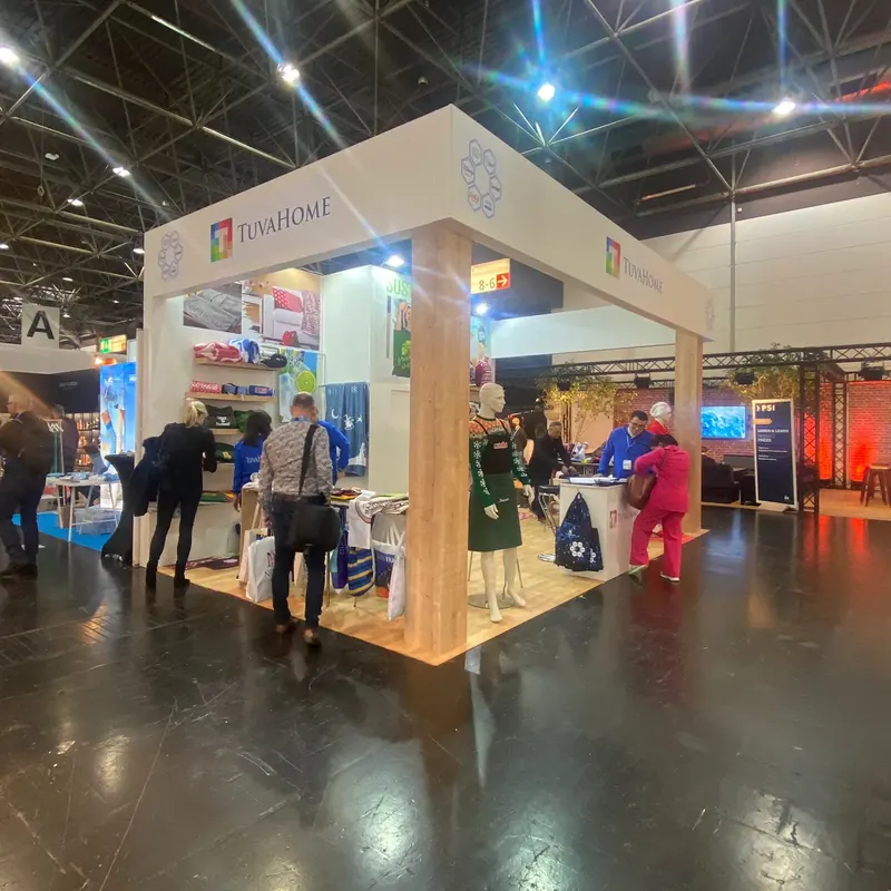 Offener Messestand mit Holzoptikrahmen, bunten Stoffmustern und Besuchern.