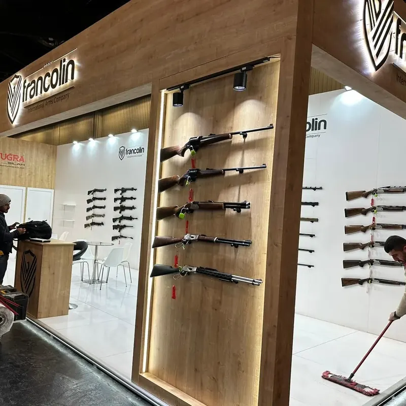 Holzverkleideter Messestand mit beleuchteter Wandnische und ausgestellten Langwaffen.