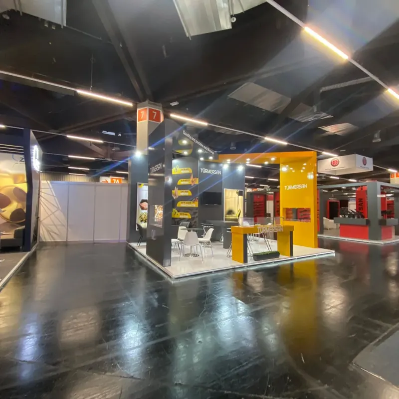 Gelb-grauer Messestand mit offenem weißem Rahmen, Produktwänden und weißen Sitzgruppen.