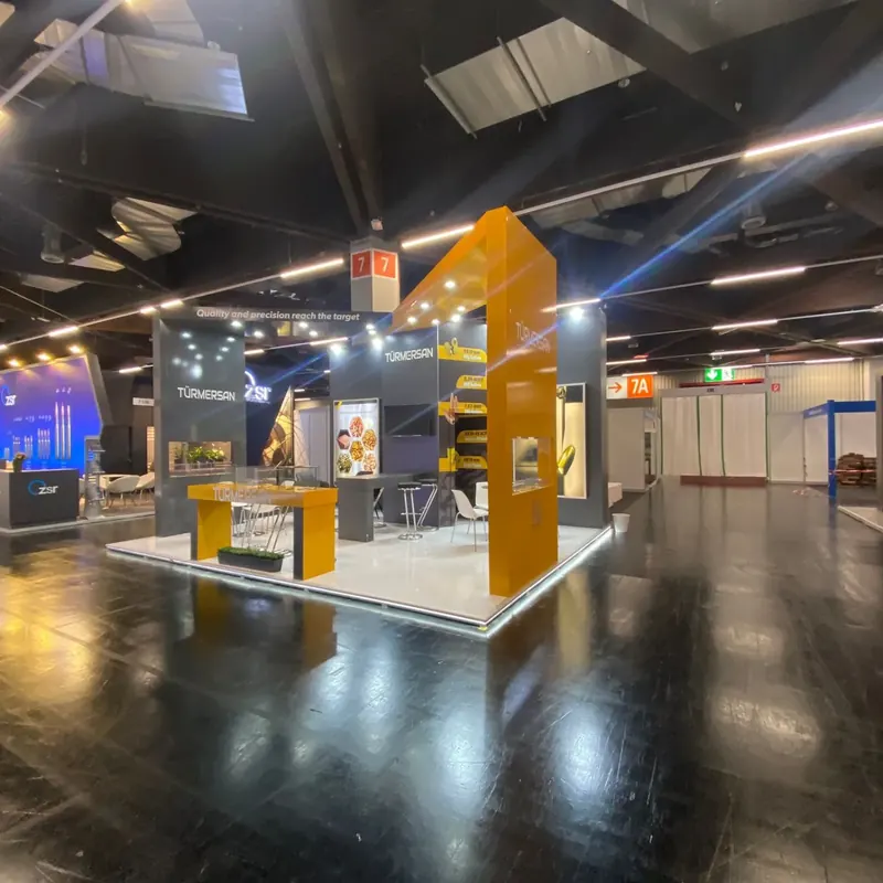 Gelb-grauer Messestand mit offenem weißem Rahmen, Produktwänden und weißen Sitzgruppen.