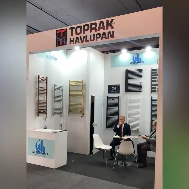 Weißer Messestand mit Heizkörpern an den Wänden, Empfangstheke und kleiner Sitzgruppe.