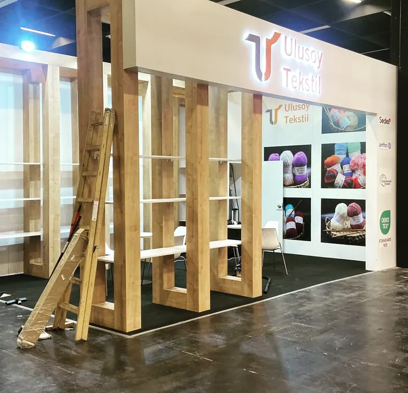 Heller Messestand mit sichtbaren Holzrahmen, senkrechten Streben und einer Leiter.