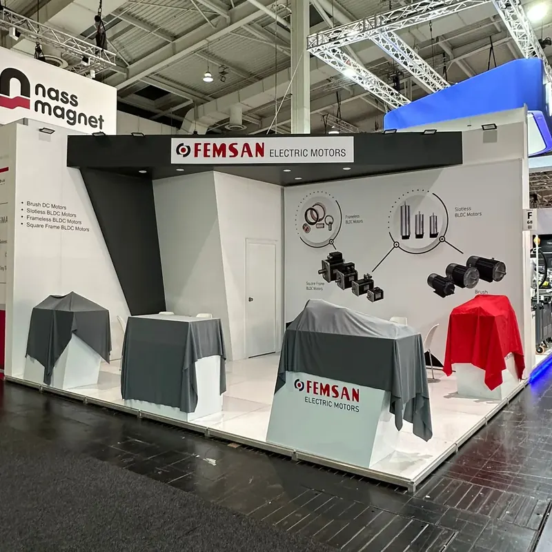 Weißer Messestand mit Technikgrafiken und mehreren grau und rot abgedeckten Exponaten.