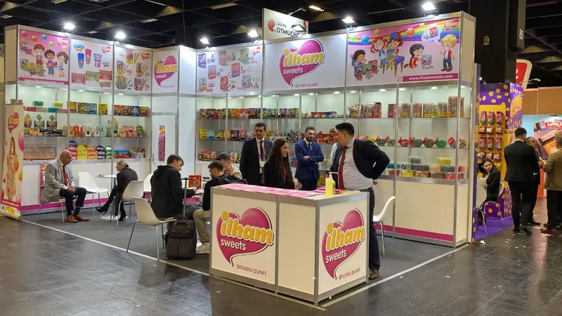 Weißer Messestand mit pinken Akzenten, Produktvitrinen und Besuchern.