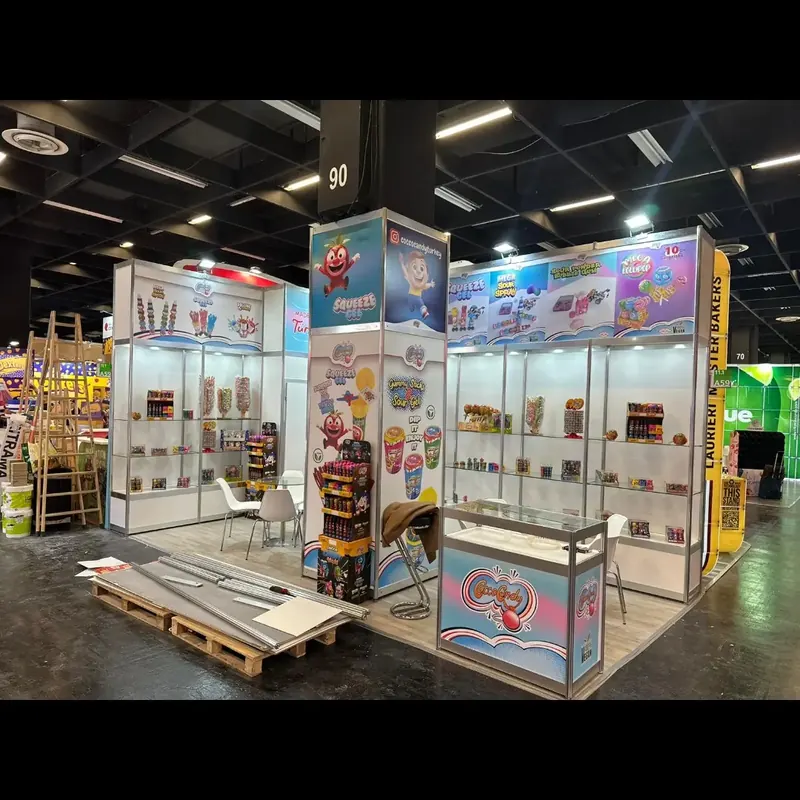 Bunter Messestand mit transparenten Produktregalen, Bildwänden und Paletten davor.