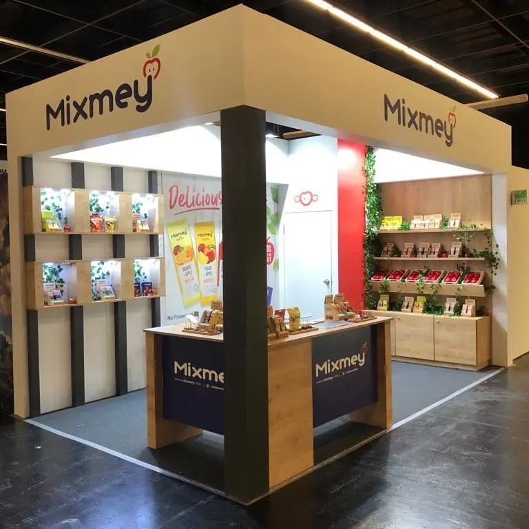 Heller Messestand mit dunklen Stützen, offenen Produktregalen und einer Holzoptiktheke.