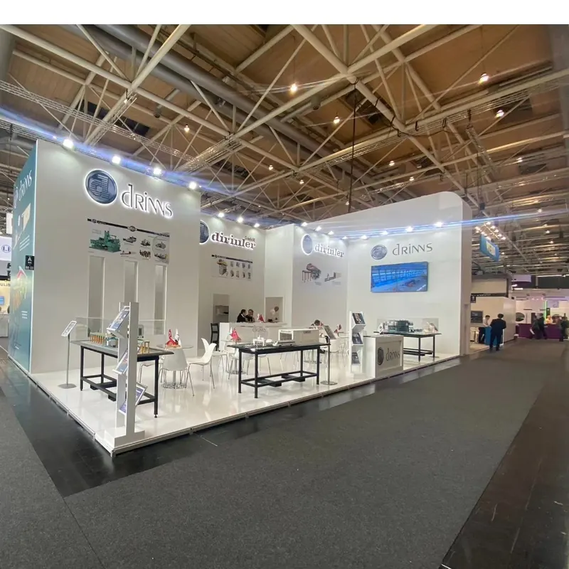 Weißer offener Messestand mit mehreren Metalltischen und großen beleuchteten Wandgrafiken.