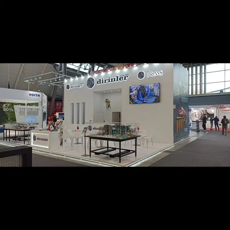Weißer Messestand mit hohen Markenwänden, Metalltischen und kleiner Sitzgruppe.