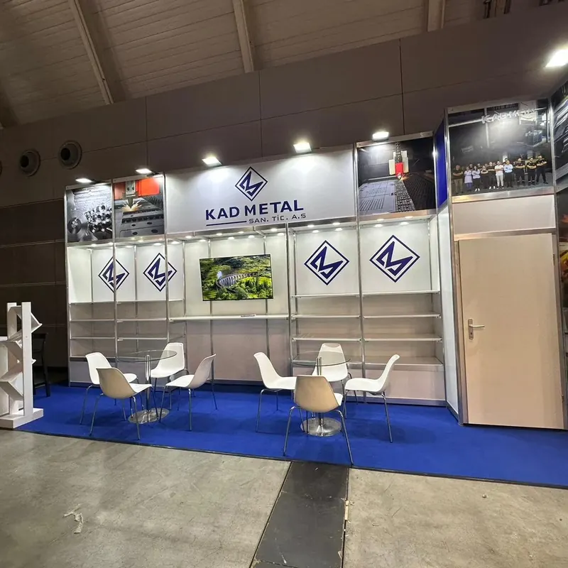 Weißer Messestand mit blauen Akzenten, Wandregalen und zwei weißen Sitzgruppen.