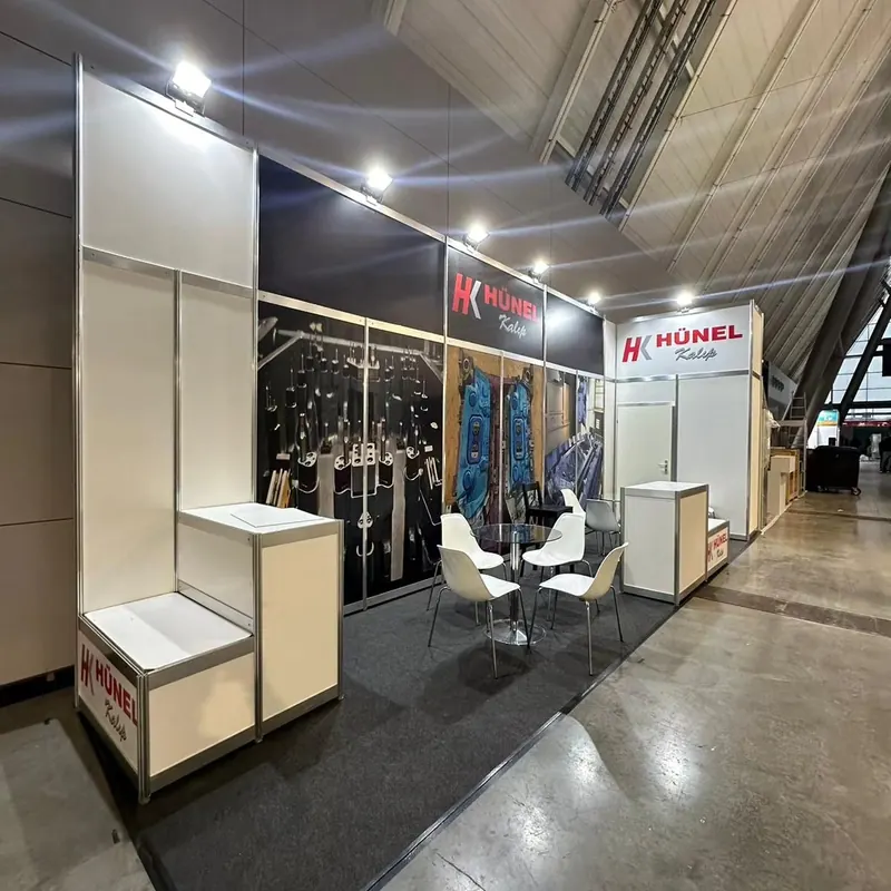 Weißer Messestand mit schwarzen Grafikwänden, Produktpodesten und weißen Stühlen.