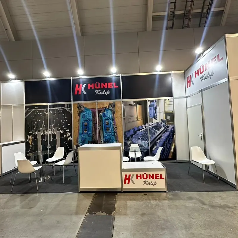 Weiß-schwarzer Messestand mit Maschinenbildern, Empfangstheke und weißen Stühlen.