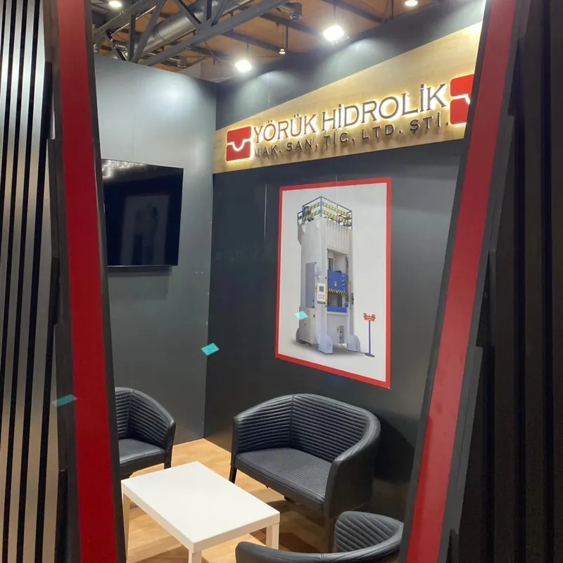 Dunkelgrauer Messestand mit roten Rahmen, schwarzen Sesseln und kleinem weißem Tisch.