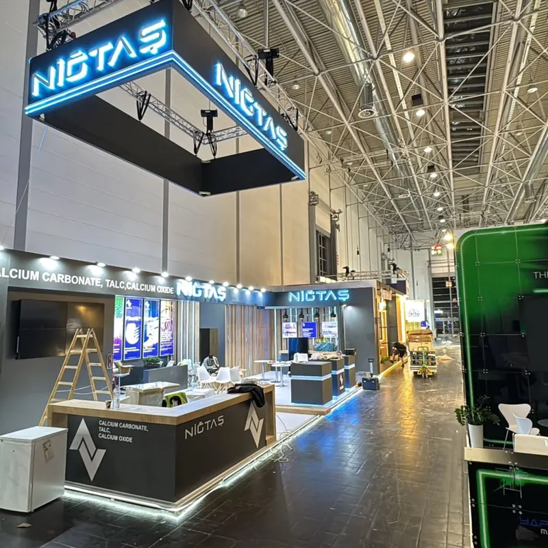 Messestand mit hohem weißem Rahmen, blauen Leuchtschriftzügen und langen Theken.