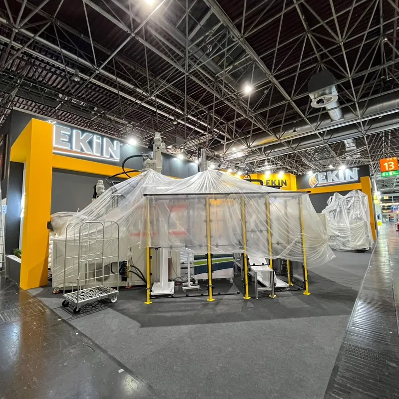 Mit Folie abgedeckte große Maschine vor einem gelb-dunkelgrauen Messestand.