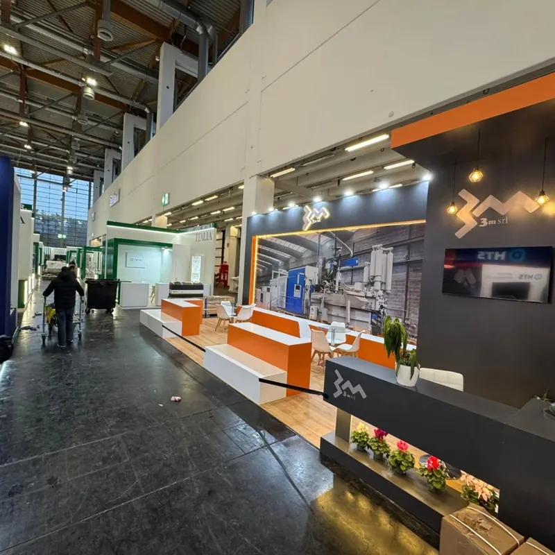 Orange-weißer Messestand mit langen Theken, Produktgrafiken und kleinen Pflanzen.