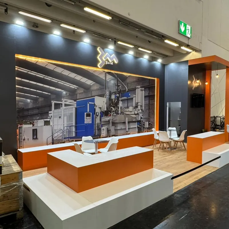 Orange-weißer Messestand mit gestaffelten Theken und großem Maschinenmotiv an der Rückwand.