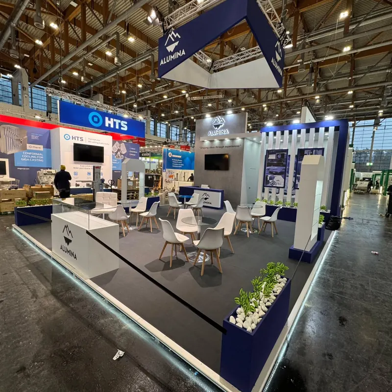 Weiß-blauer Messestand mit abgehängtem Rahmen, Sitzgruppen und Produktpodesten.