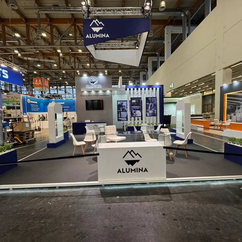 Weiß-blauer Messestand mit abgehängtem Rahmen, Sitzgruppen und Produktpodesten.