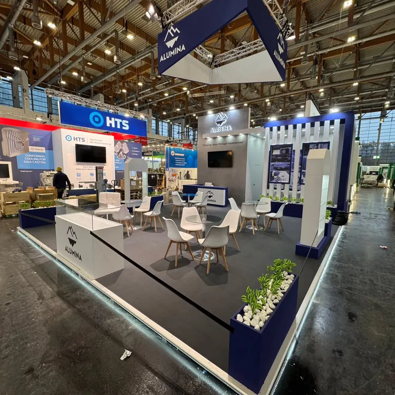 Weiß-blauer Messestand mit abgehängtem Rahmen, Sitzgruppen und Produktpodesten.