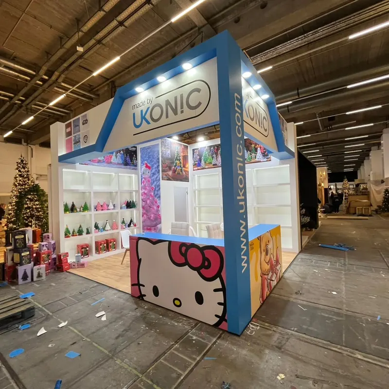 Blau-weißer Messestand mit bunten Figurenmotiven und offenen Produktregalen.