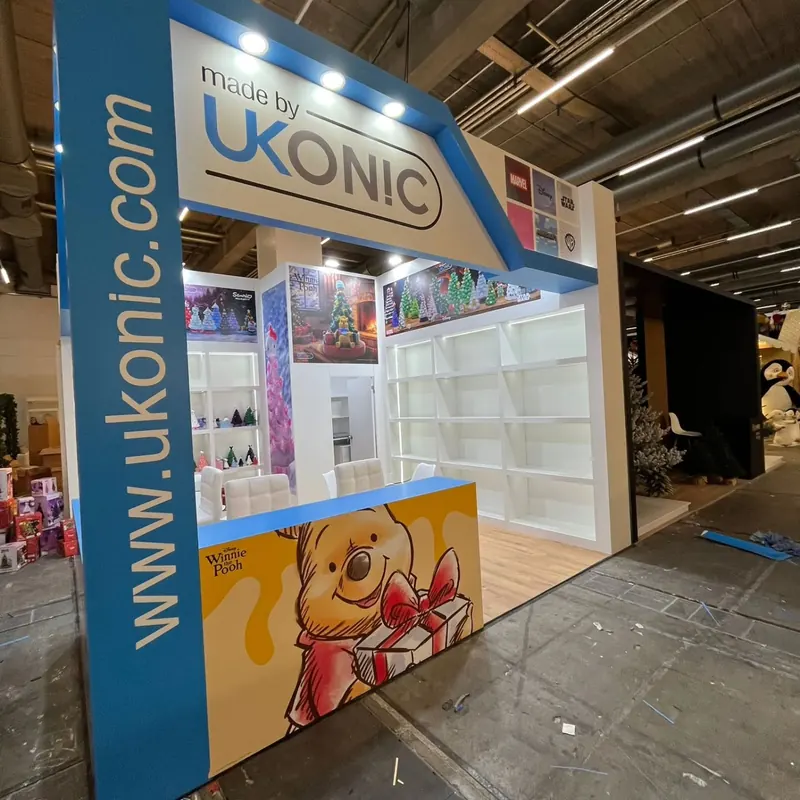 Blau-weißer Messestand mit bunten Figurenmotiven und offenen Produktregalen.
