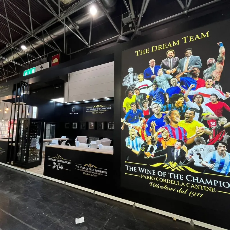 Schwarzer Messestand mit großer Bildwand, beleuchteten Regalen und einer Theke.