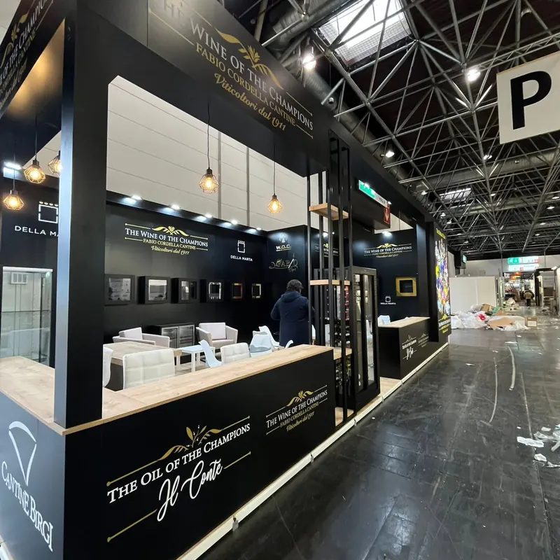 Schwarz-goldener Messestand mit langer Theke, Pendelleuchten und senkrechten Lamellen.
