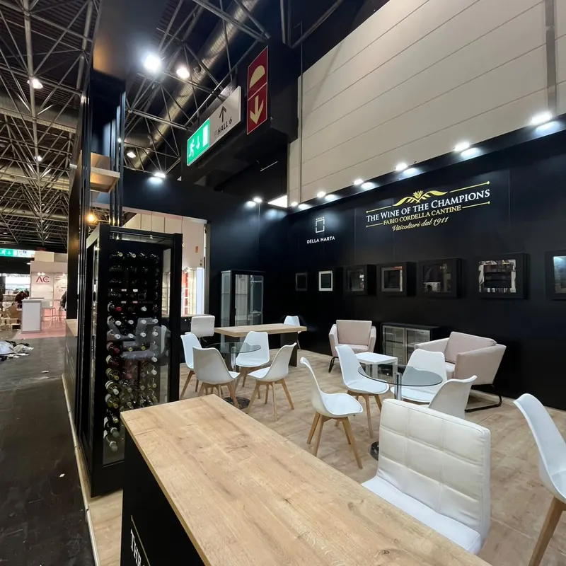 Schwarzer Messestand mit hellen Sitzgruppen, weißen Sesseln und Holztischen.