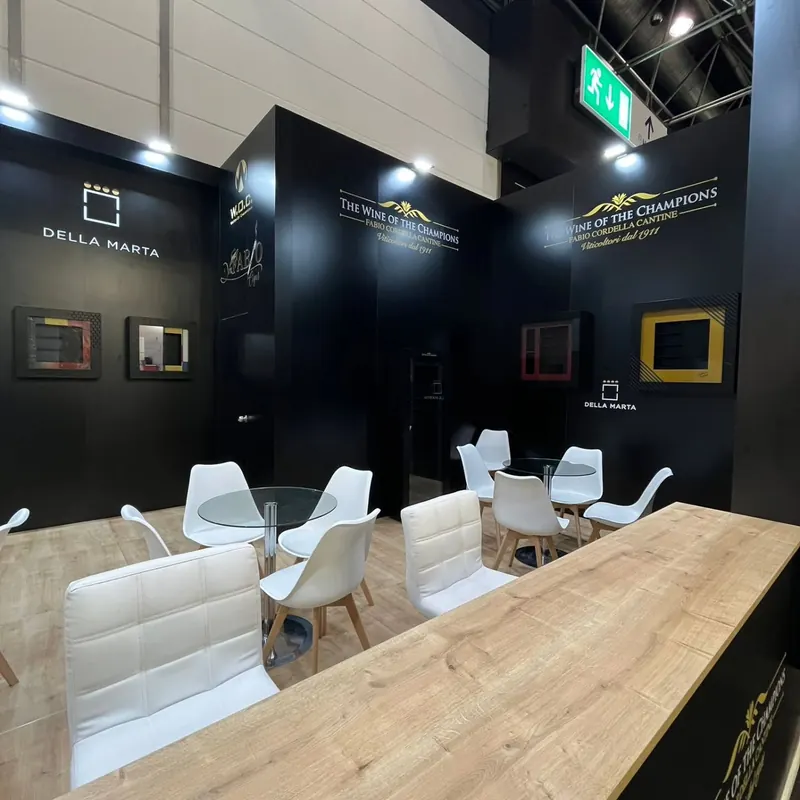 Dunkler Messestand mit eingerahmten Produktpräsentationen, weißen Sesseln und Holztheke.