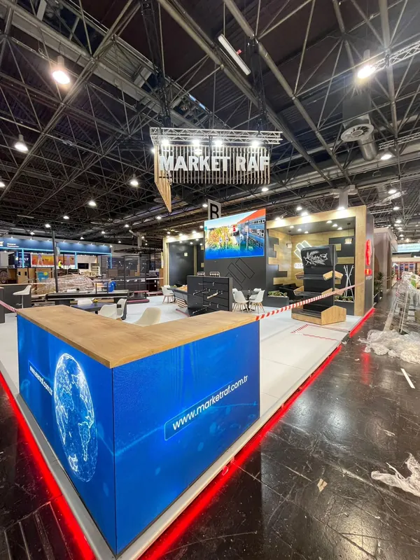 Blaue Theke mit Holzplatte vor Maschinenexponaten und rot beleuchteter Standkante.