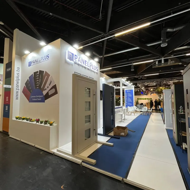 Weißer Messestand mit Türmustern, beleuchteter Beschriftung und blauem Gang.