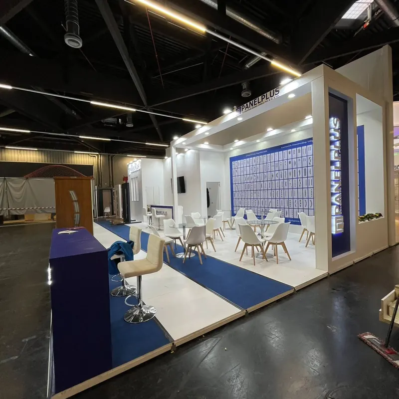 Heller weißer Messestand mit blauem Teppichstreifen und weißen Sitzgruppen.