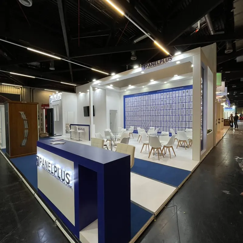 Heller weißer Messestand mit blauem Teppichstreifen und weißen Sitzgruppen.