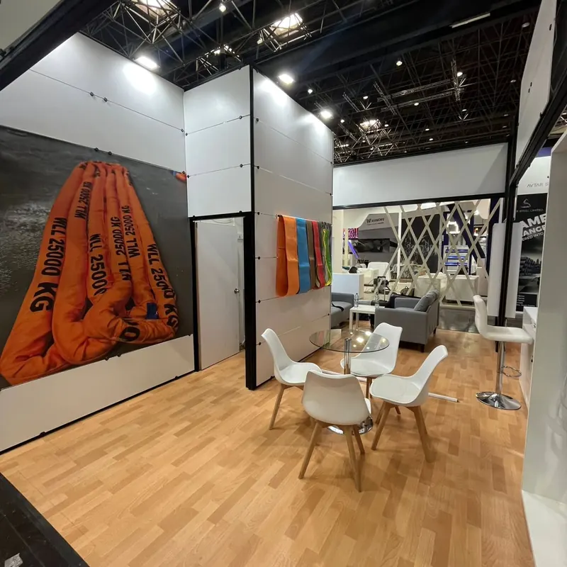 Weißer Messestand mit großem orangefarbenem Produktmotiv, Holzboden und weißen Stühlen.