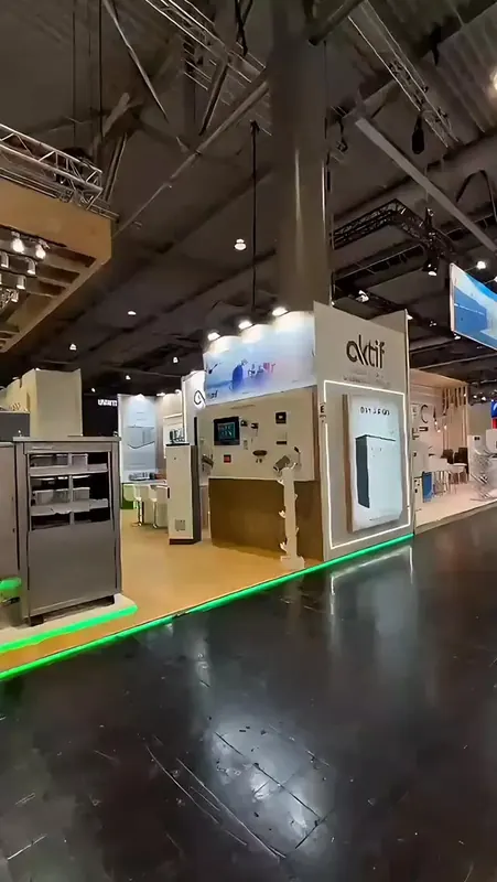 Reel-Vorschaubild: Messestand mit Produktmodulen, Holzdetails und grüner Beleuchtung am Bodenrand.