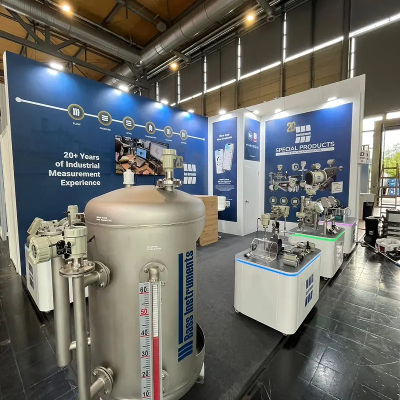 Blau-weißer Messestand mit großen Metallbehältern und Technikexponaten auf Podesten.