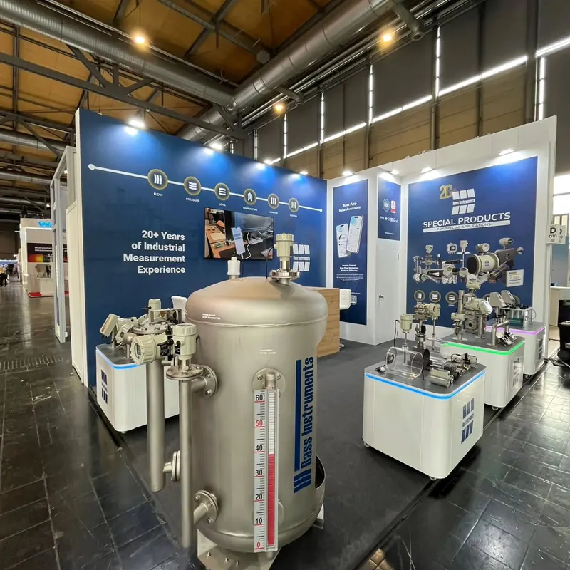 Zylindrischer Metallbehälter vor weißen Maschinenpodesten und blauer Informationswand.