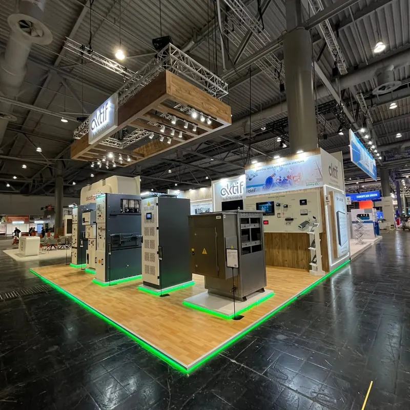 Messestand mit Holzfußboden, grüner Lichtkante, Technikexponaten und einer abgehängten Holzblende.