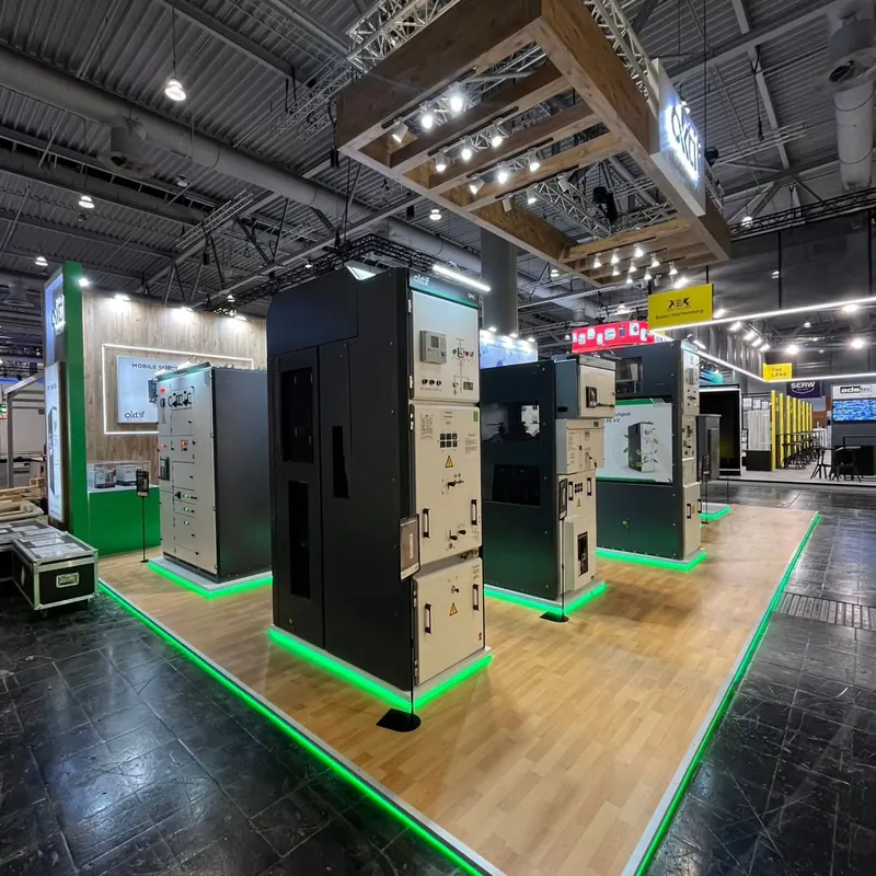 Schwarz-weißer Messestand mit hohen Produktpodesten, grün beleuchteten Bodenkanten und Holz-Deckenrahmen.