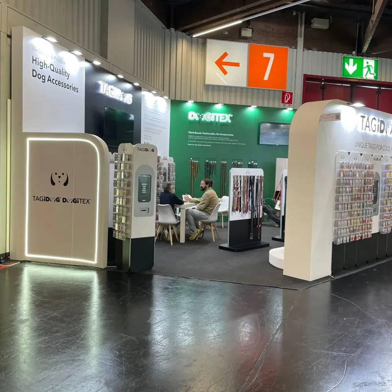 Weiß-grüner Messestand mit leuchtendem Rahmen, Produktständern und Sitzbereich.
