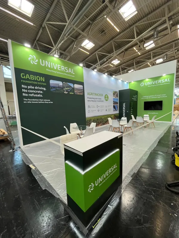 Grün-weißer Messestand mit heller Theke, Produktgrafiken und kleinen Besprechungstischen.