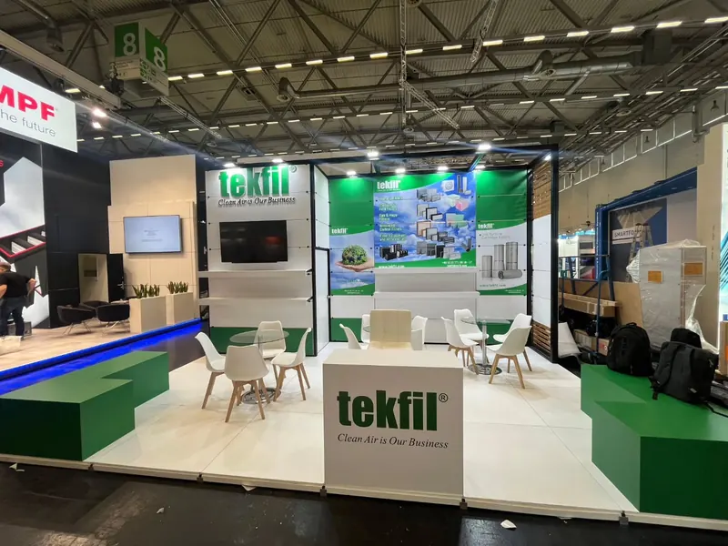 Grün-weißer Messestand mit Empfangstheke, Produktgrafik und mehreren weißen Sitzgruppen.
